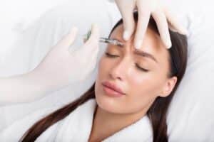 Young woman recieving injection of anti-aging botox filler to forehead from professional cosmetologist in beauty salon