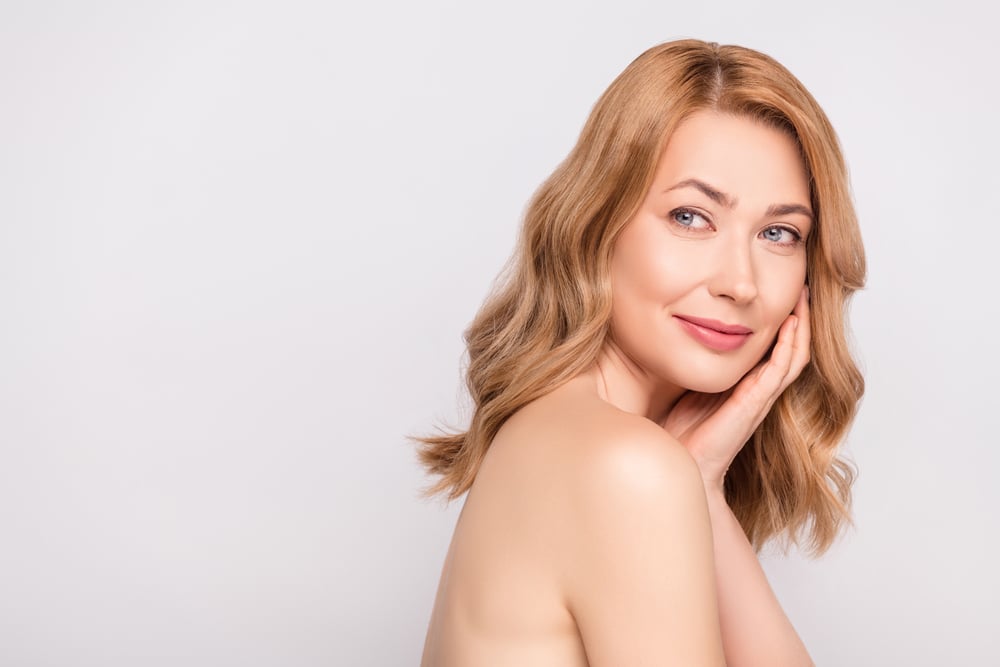 Beautiful young woman smiling and touching her face confidently after receiving facial plastic surgery.