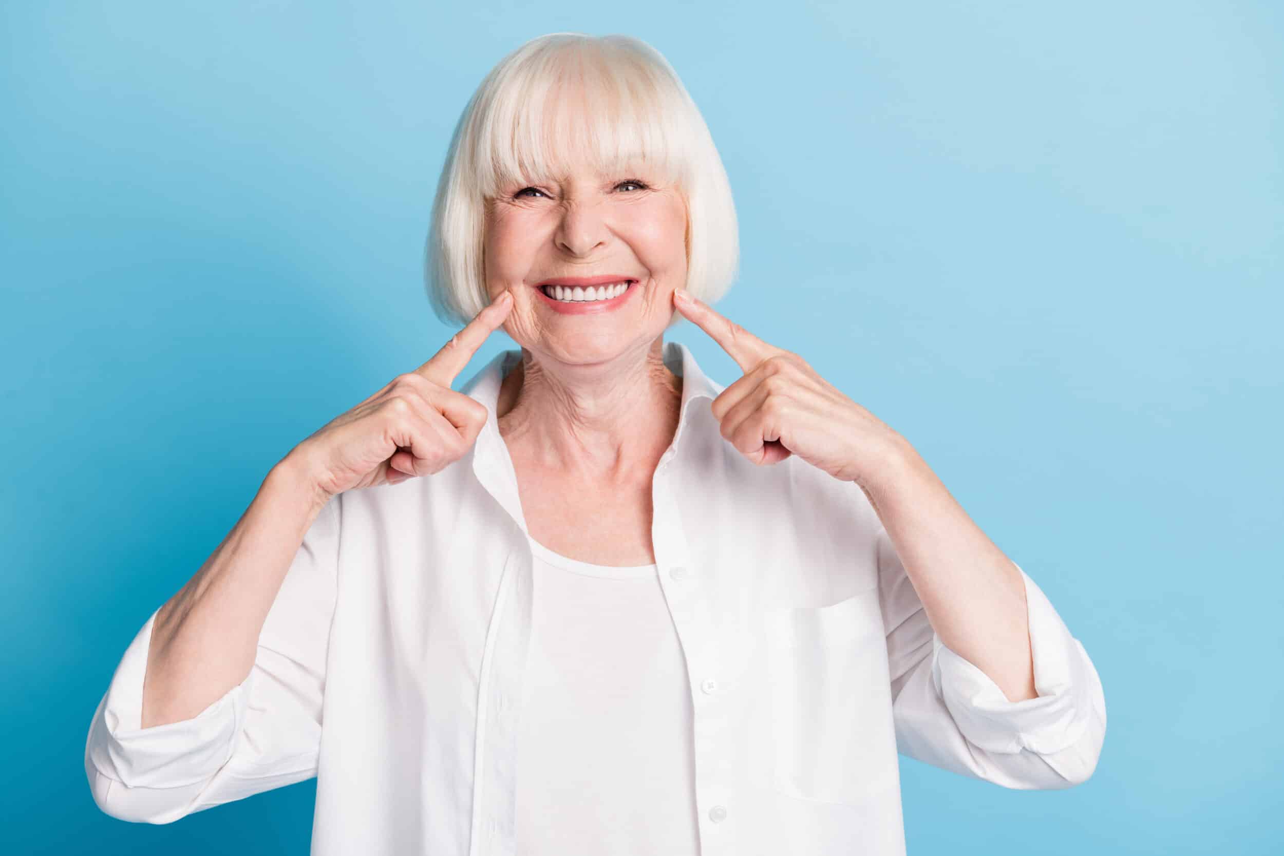 Older woman smiling and pointing to the wrinkles around her mouth, in need of treatment