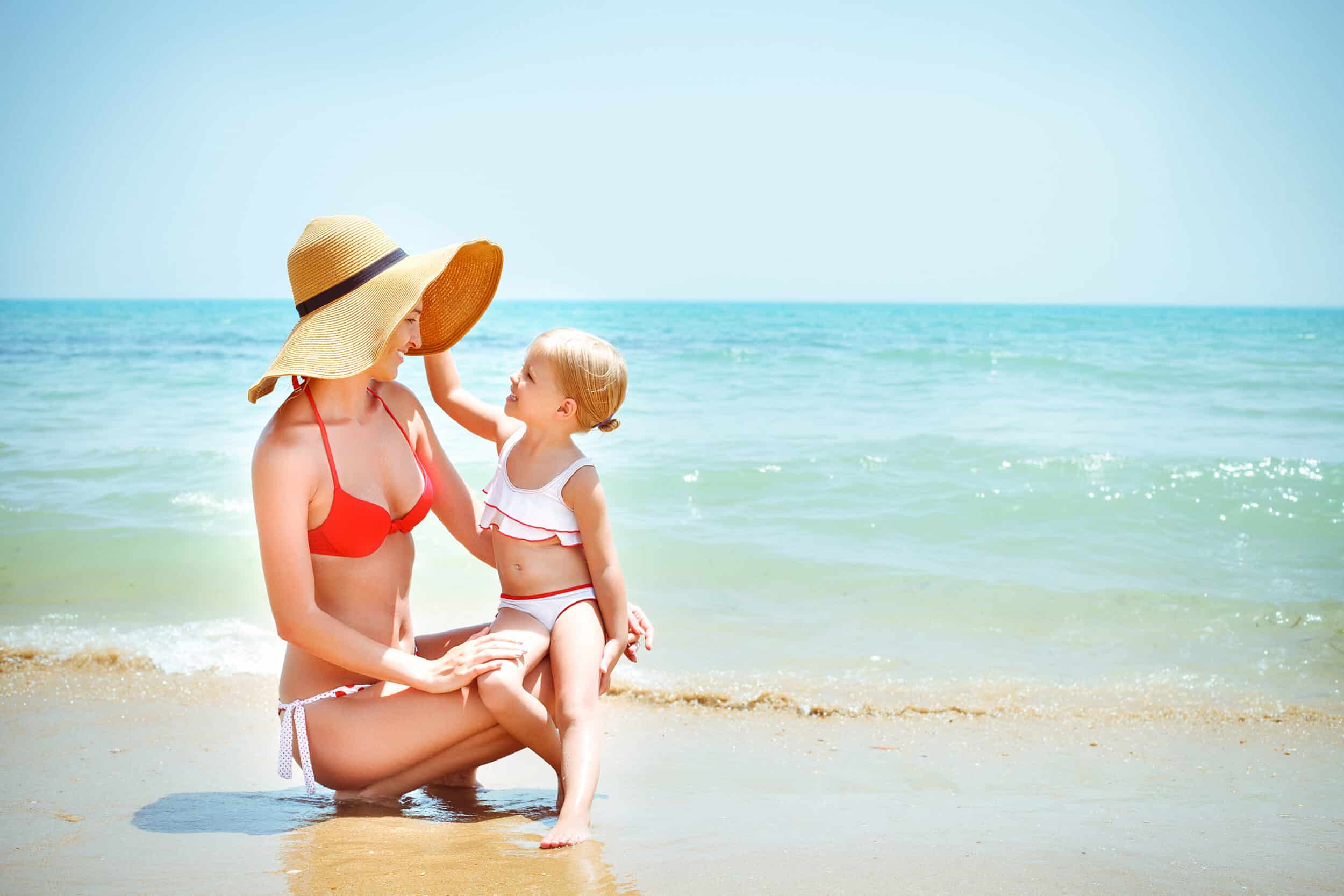 Fit young mom on the beach with her child, confident after her mommy makeover