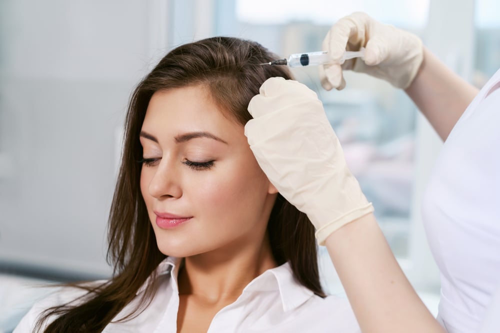 Happy woman receiving PRP hair restoration injections to her scalp to promote growth.