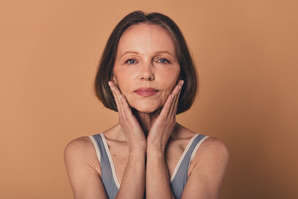 Older woman holding her sharpened, defined jawline after getting a facelift to restore her youthful features.