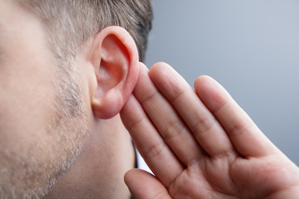Close up of a man pushing his ear forward in self-consciousness, perhaps in need of Otoplasty.